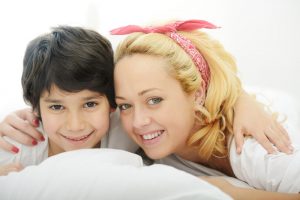Happy blonde young mother with her son in bedroom bed