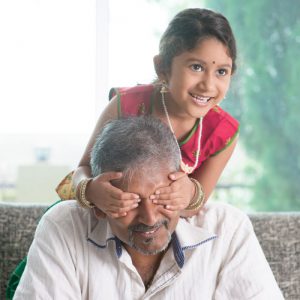 Happy Indian family at home. Asian girl surprising her father by covering dad eyes. Parent and child indoor lifestyle.